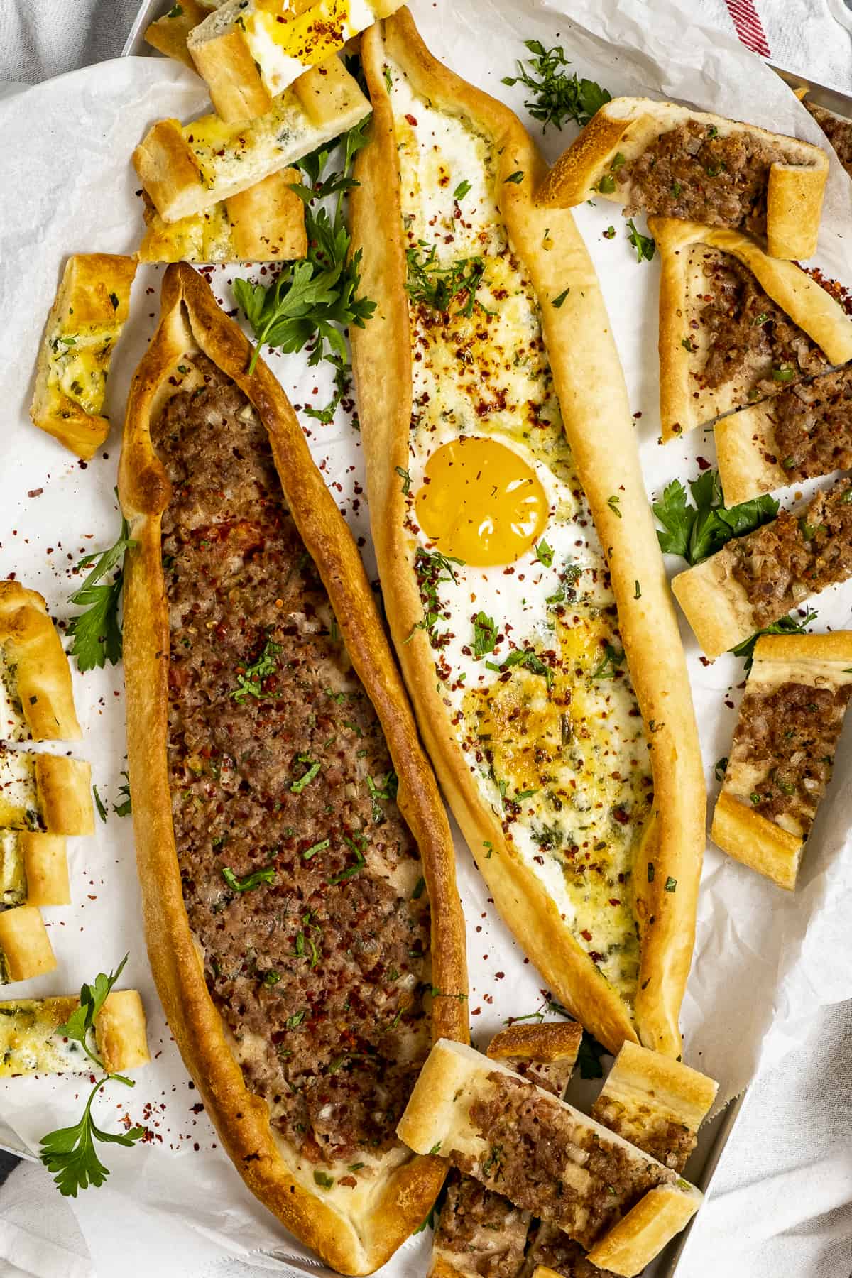 Two whole Turkish pide, one topped with an egg and slices of pide around them.