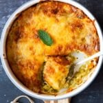 Golden top cheesy zucchini casserole in a white round pan with a spoon in it.