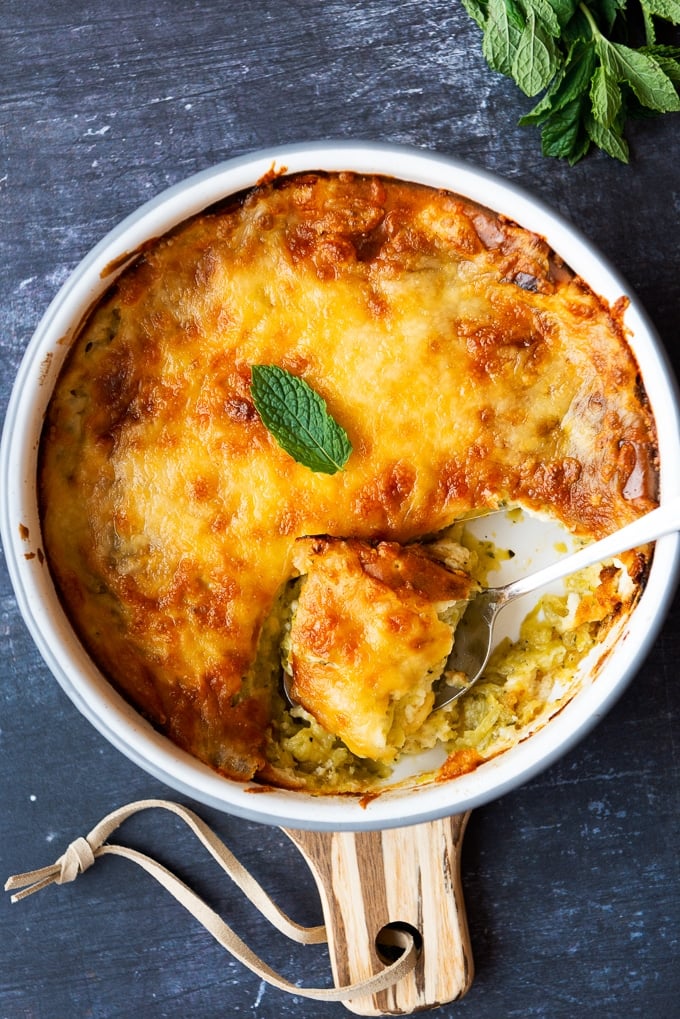 Cheesy zucchini casseole in a round pan with a spoon inside it.