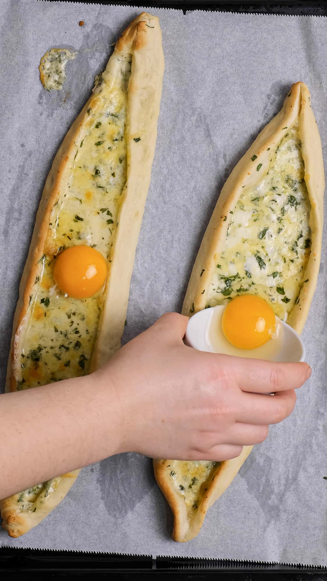 A hand placing eggs on two half cooked cheese pides.