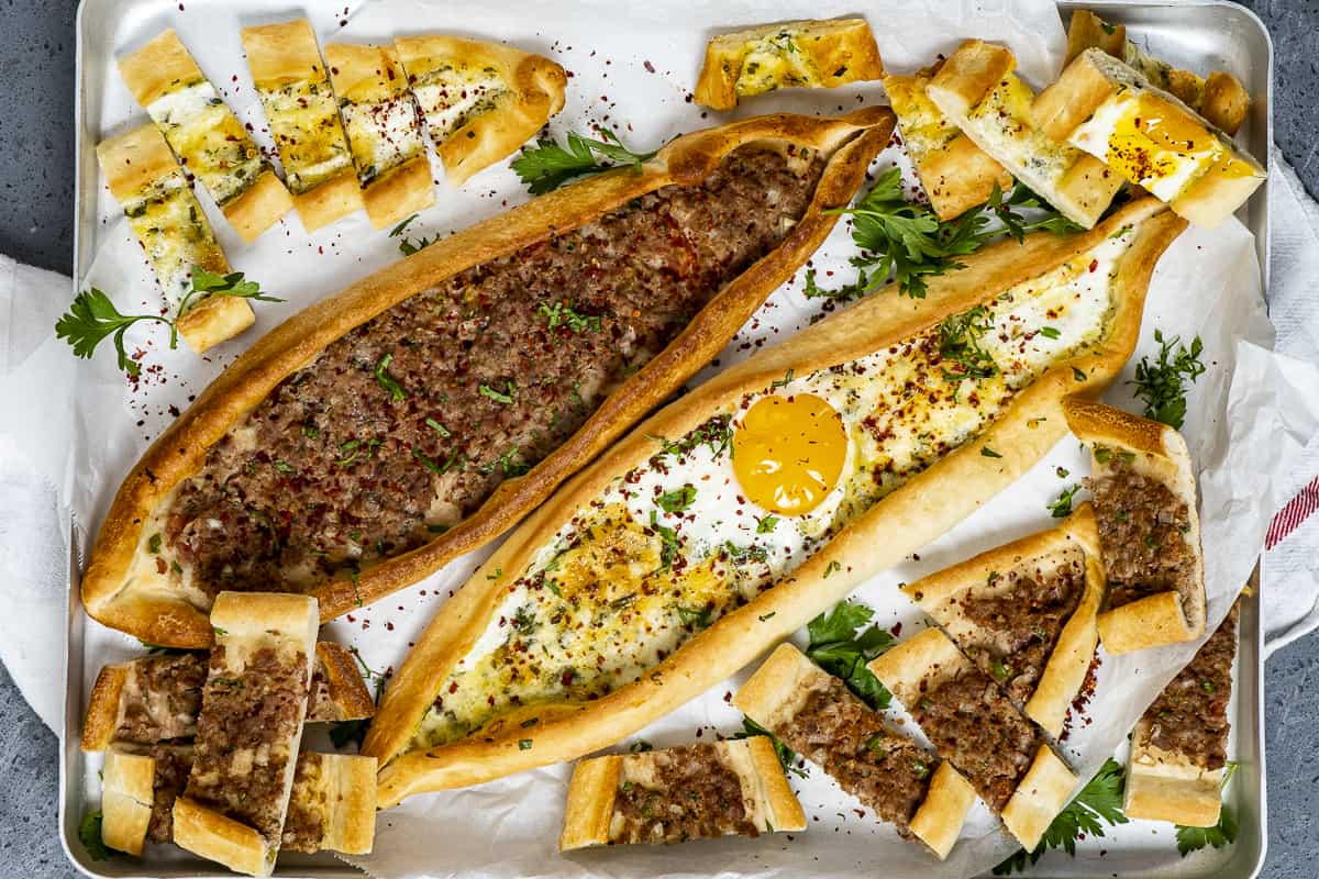 Turkish pizza pide garnished with parsley and red pepper flakes and served in a baking tray.