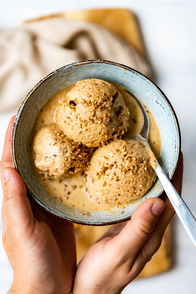 Holding a bowl of almond milk ice cream with tahini and sesame seeds with a spoon.