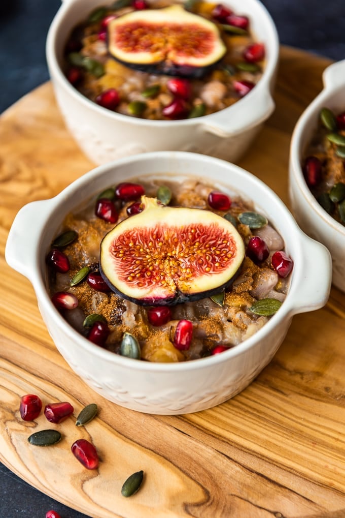 Ashura dessert with grains and fruit in white bowls on a wooden board.