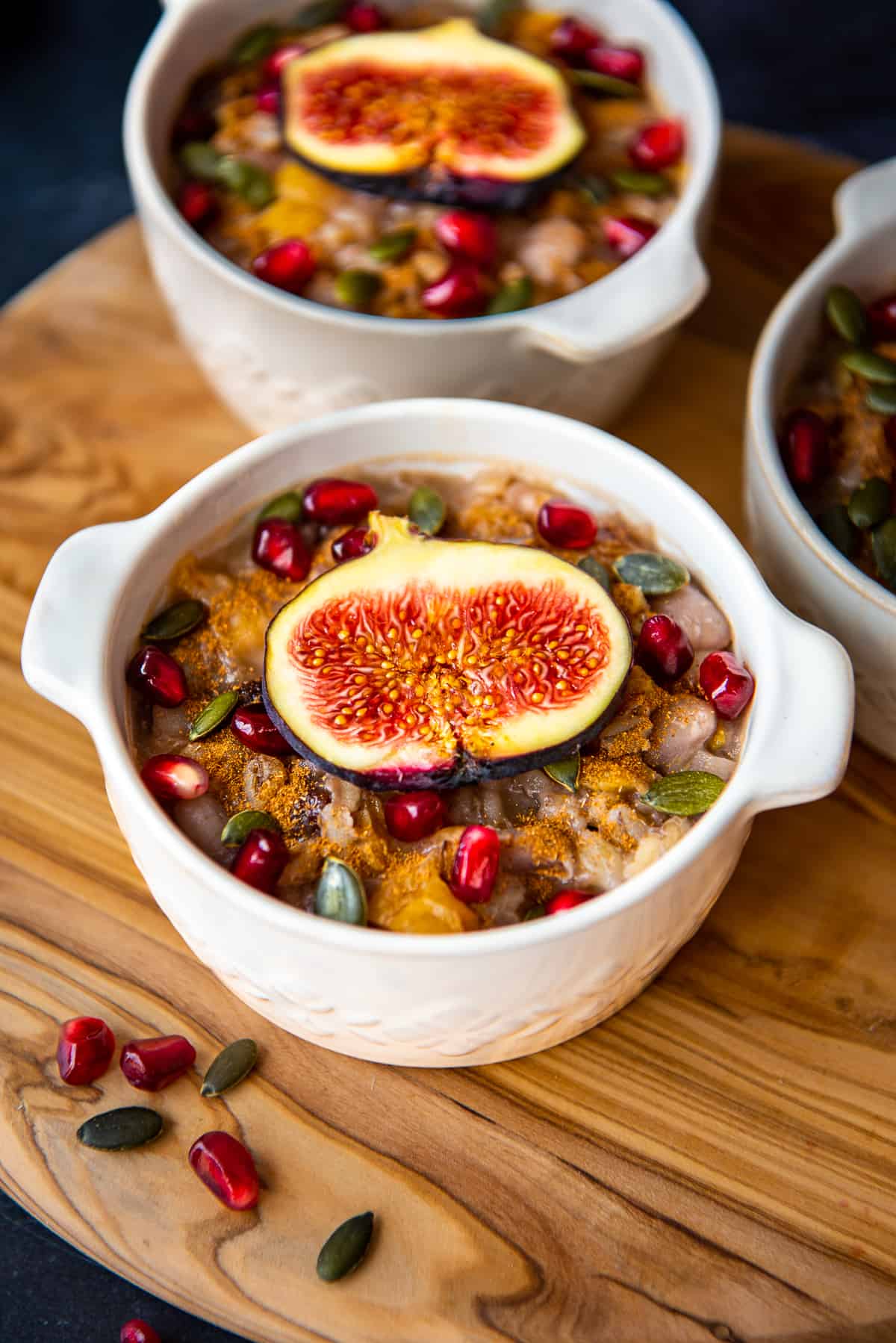 Ashure topped with figs and pomegranate arils in white bowls.
