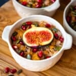 Ashure pudding topped with figs and pomegranate seeds in a white bowl.