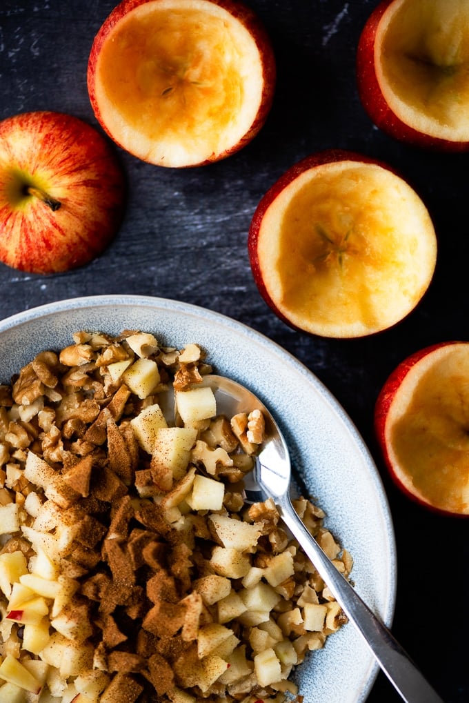 Apples scooped out and ready to be stuffed with walnuts on a dark background.