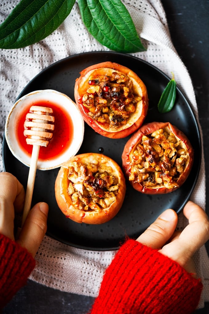 Woman with a red jumper serving baked whole apples with walnuts and beet syrup on a dark plate