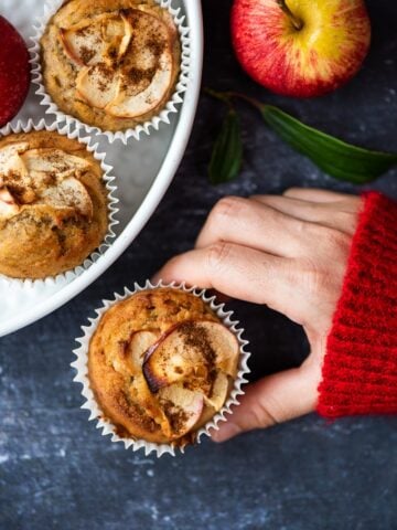 Woman's hand holding an apple muffin and a red apple accompanies