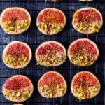 Tahini dipped fresh figs garnished with pistachio and sesame seeds on a dark background.