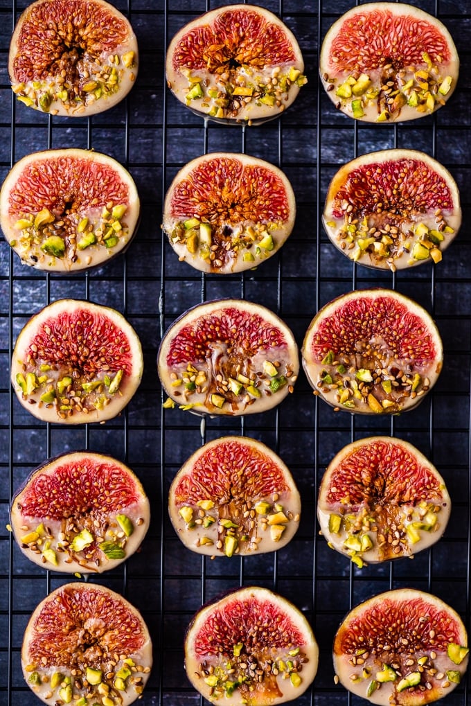 Fresh figs dipped into tahini, sweetened with date molasses, garnished with pistachios and sesame seeds on a background.