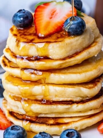 Fluffy almond milk pancakes stacked on a plate, topped with fresh strawberries, blueberries and drizzled with maple syrup.
