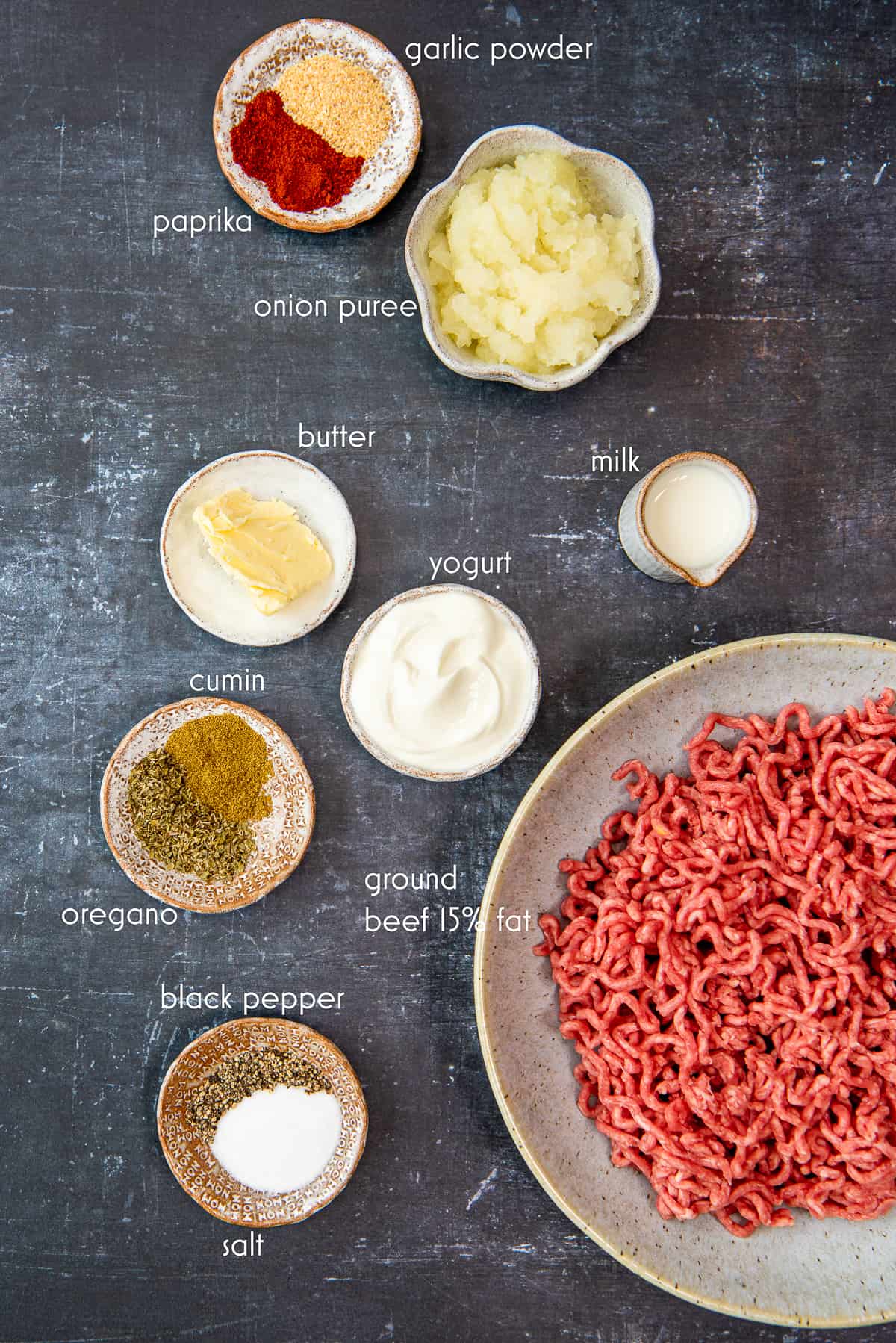 Ground beef, pureed onion, milk, yogurt, butter and spices photographed on a dark background.