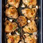 Golden and crispy skin baked chicken pieces with garlic and rosemary in a roasting pan.