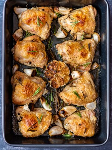 Golden and crispy skin baked chicken pieces with garlic and rosemary in a roasting pan.
