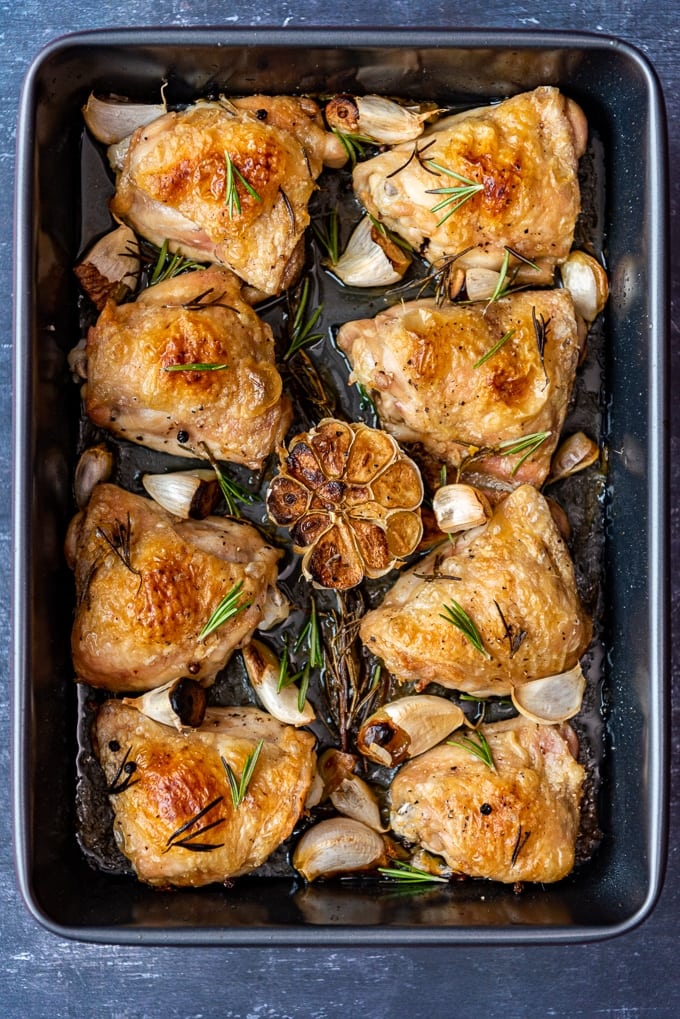 Golden and crispy skin baked chicken thighs with garlic and rosemary in a rectangular pan