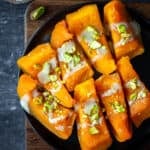 Pumpkin dessert drizzled with tahini and garnished with chopped pistachios on a black plate.
