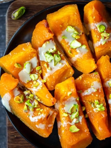 Pumpkin dessert drizzled with tahini and garnished with chopped pistachios on a black plate.