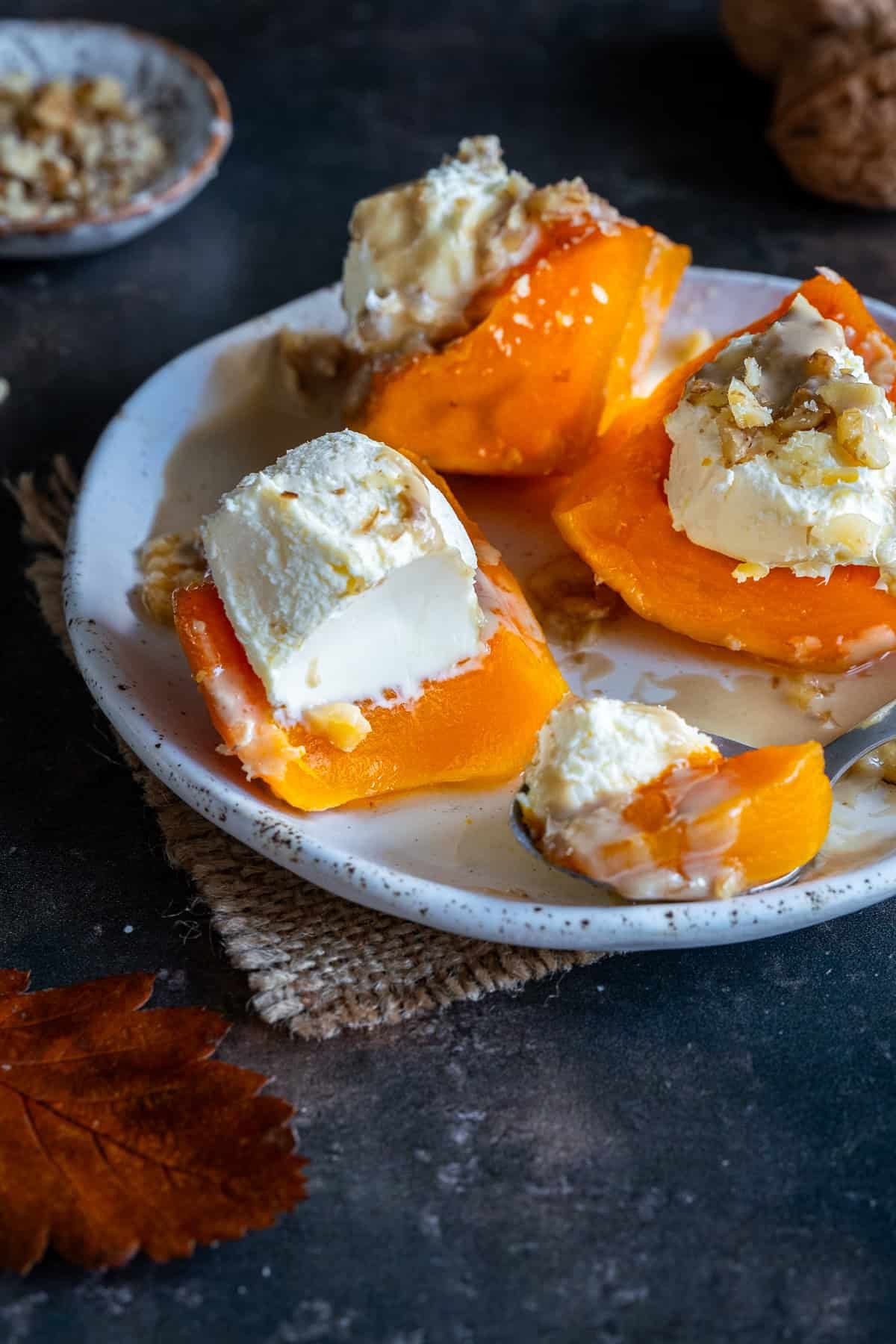Close-up of Turkish Pumpkin Dessert (Kabak Tatlısı) served on a plate with clotted cream, crushed walnuts, and syrup drizzled on top.