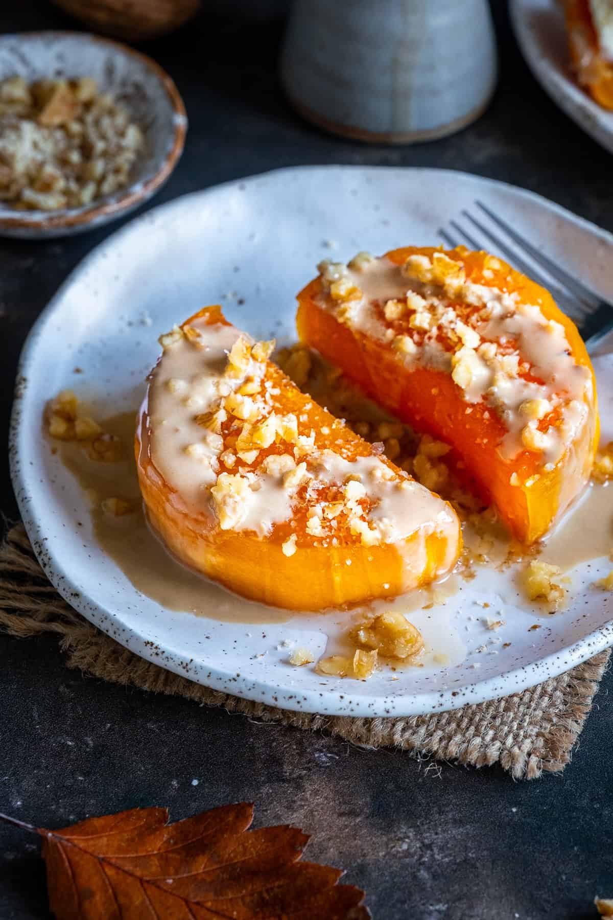 Close-up of Turkish Pumpkin Dessert (Kabak Tatlısı) topped with tahini and chopped walnuts, served on a white plate with syrup.