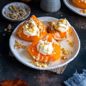 Turkish Pumpkin Dessert (Kabak Tatlısı) on a white plate, topped with clotted cream, tahini drizzle, and chopped walnuts.