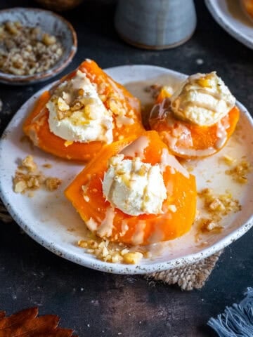 Turkish Pumpkin Dessert (Kabak Tatlısı) on a white plate, topped with clotted cream, tahini drizzle, and chopped walnuts.