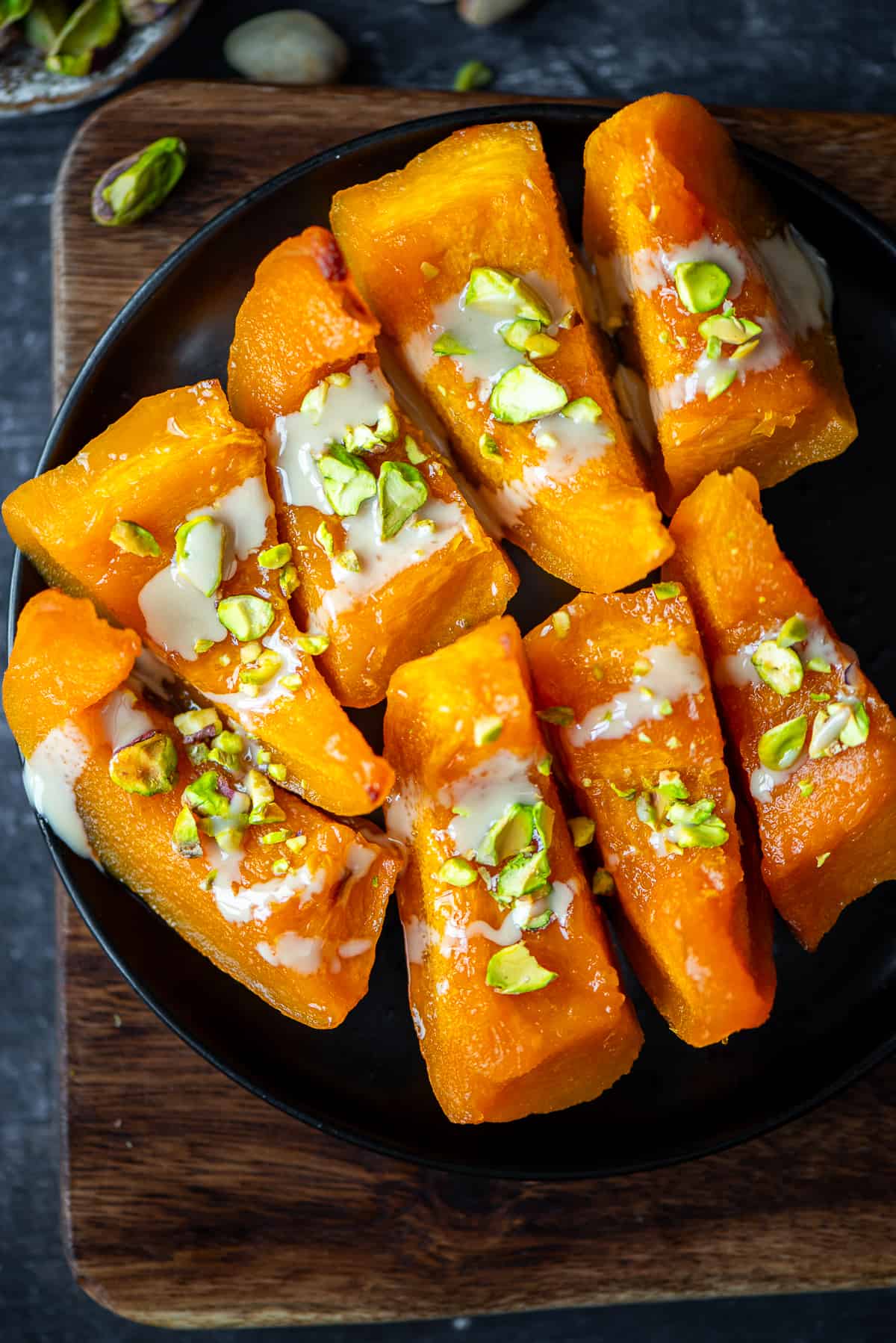 Pumpkin dessert garnished with tahini and chopped pistachios on a black plate.