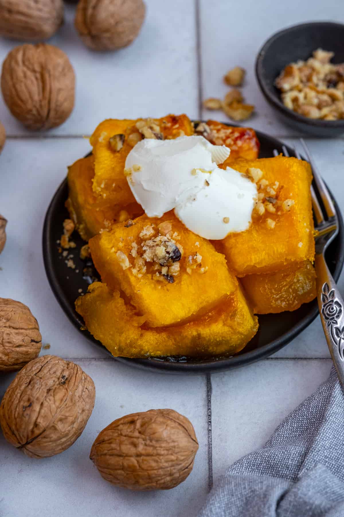 Pumpkin dessert topped with kaymak and walnuts on a black plate.