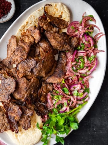 Doner kebap served with sumac onions and parsley on an oval plate.