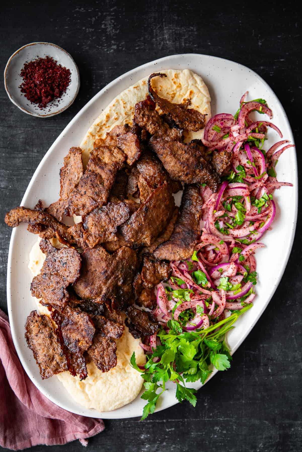 Doner kebab slices served with sumac onions and parsley on a white plate.