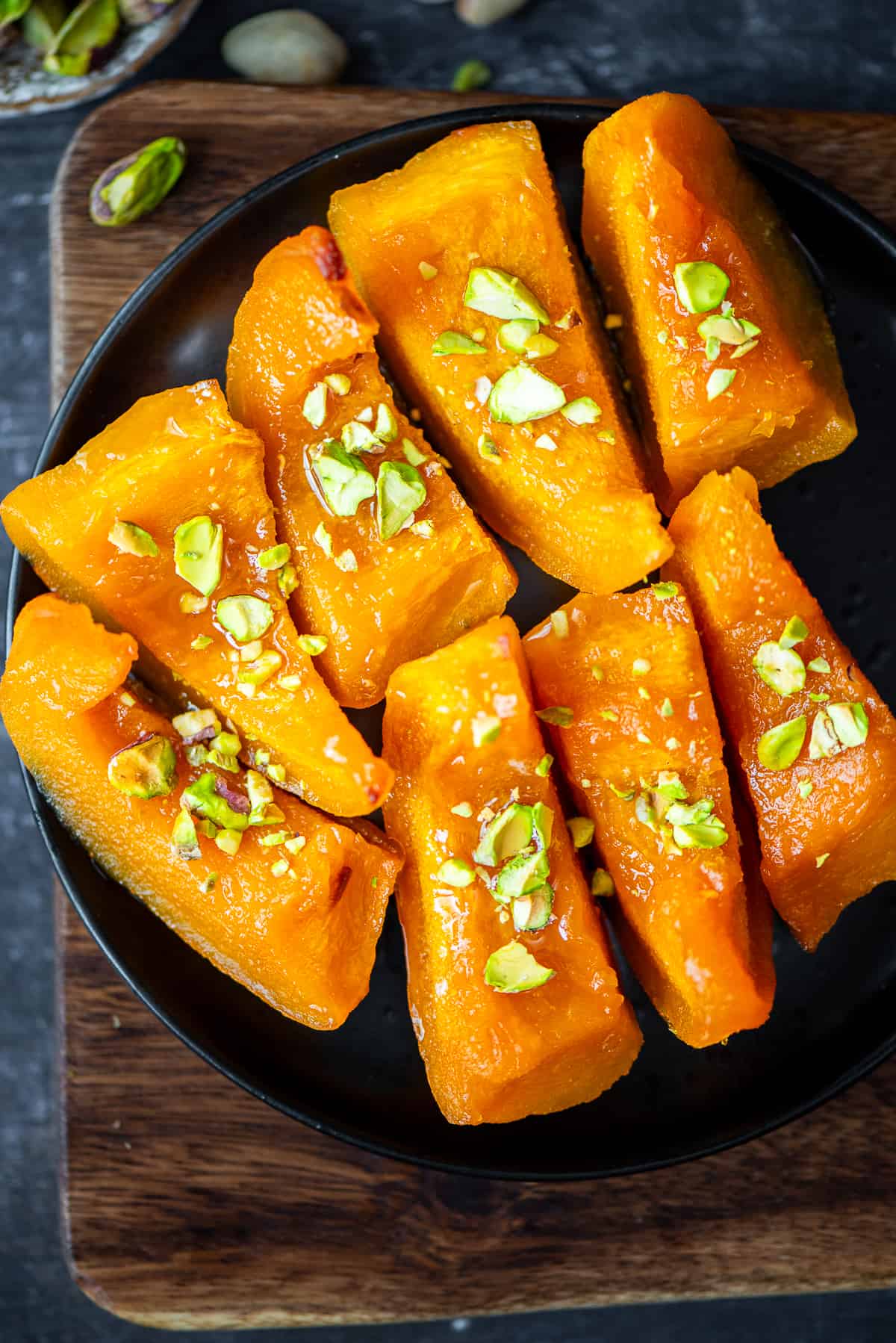 Pumpkin dessert slices garnished with chopped pistachios on a black plate.