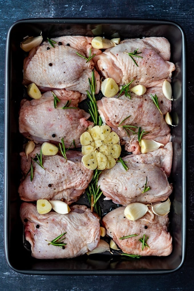 Chicken thighs with garlic and rosemary in a baking pan ready to go into the oven