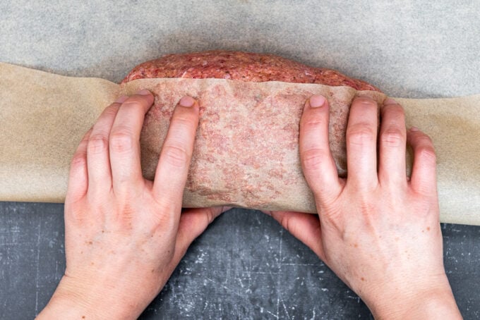 Hands wrapping a log of doner kebab meat with brown baking paper.