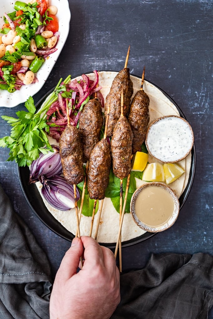 Beef and lamb koftas on skewers served on lavash with onions and herbs.