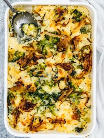 Broccoli and cauliflower casserole with cheese and crispy onion topping in a white pan with a spoon in it.