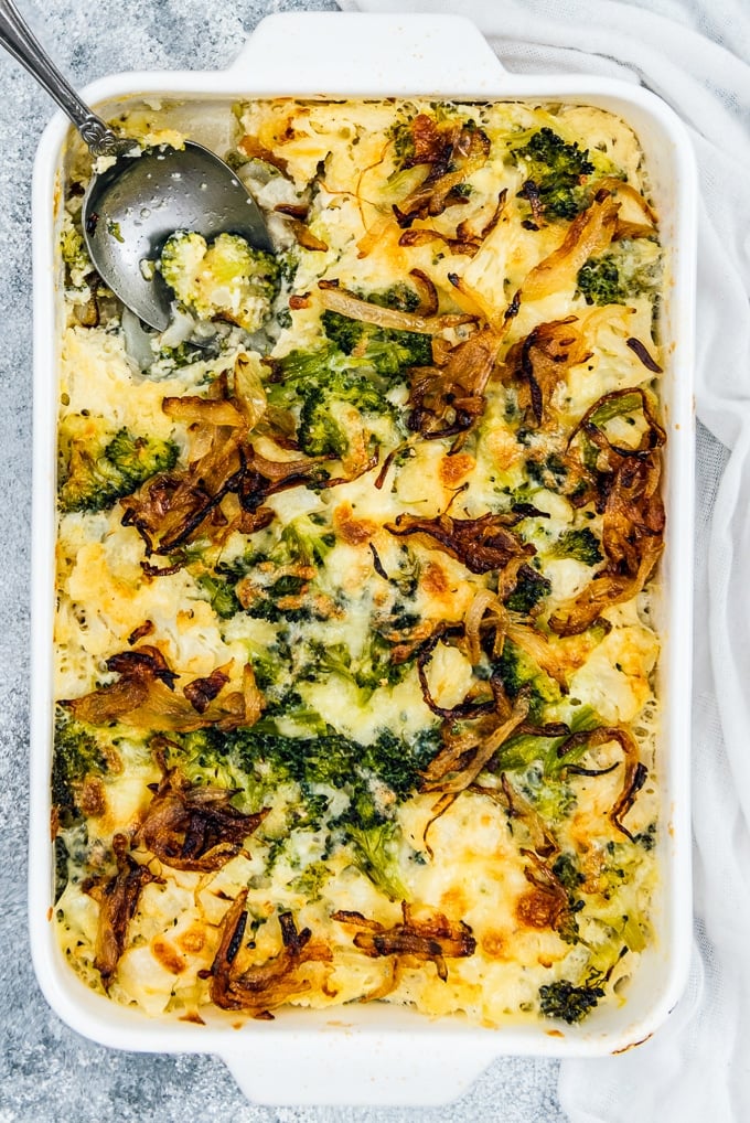 Broccoli And Cauliflower Casserole with cheese and crispy onion topping in a white pan with a spoon in it