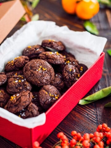 A Christmas gift box full of chocolate citrus cookies accompanied by pine tree branches, Christmas flowers and mandarins.