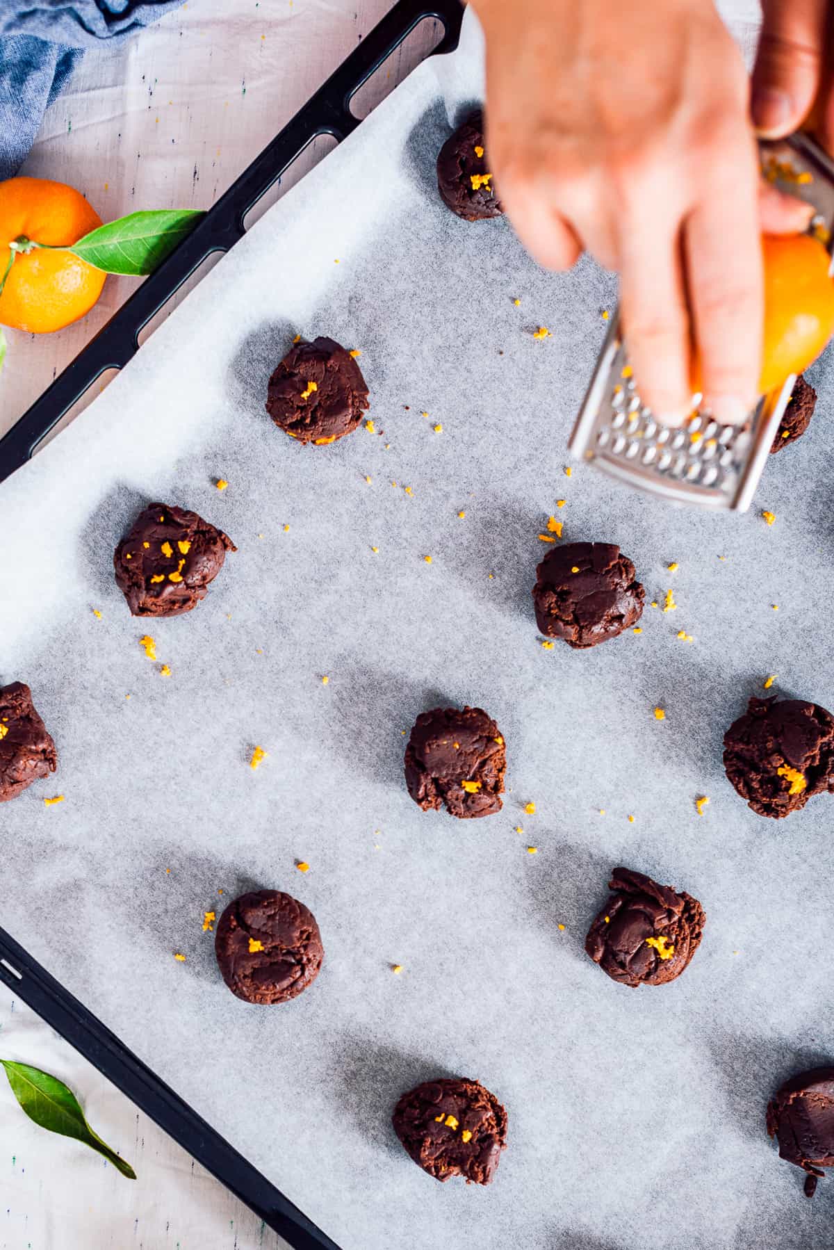 Hands grating orange zest over chocolate cookie dough balls.