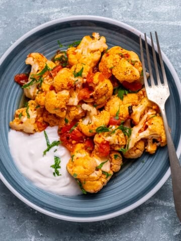 Baked cauliflower casserole with a tomato sauce served on a plate with some yogurt on the side.