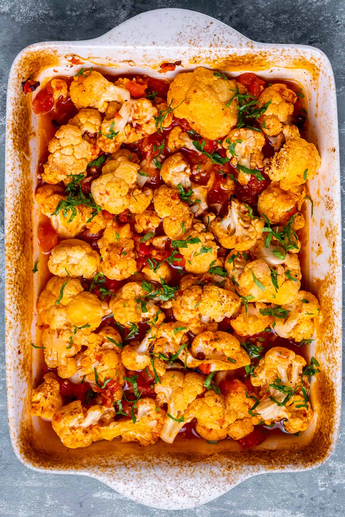 Baked cauliflower casserole with a gralicky tomato sauce in a white baking pan.