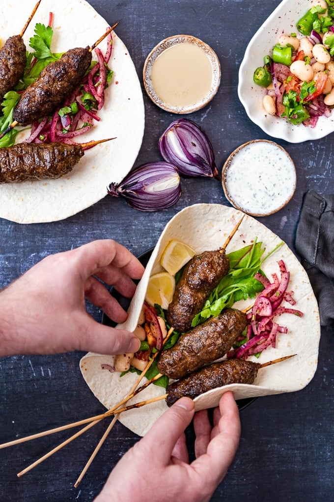 Holding kofta skewers on lavash with onions and salad.