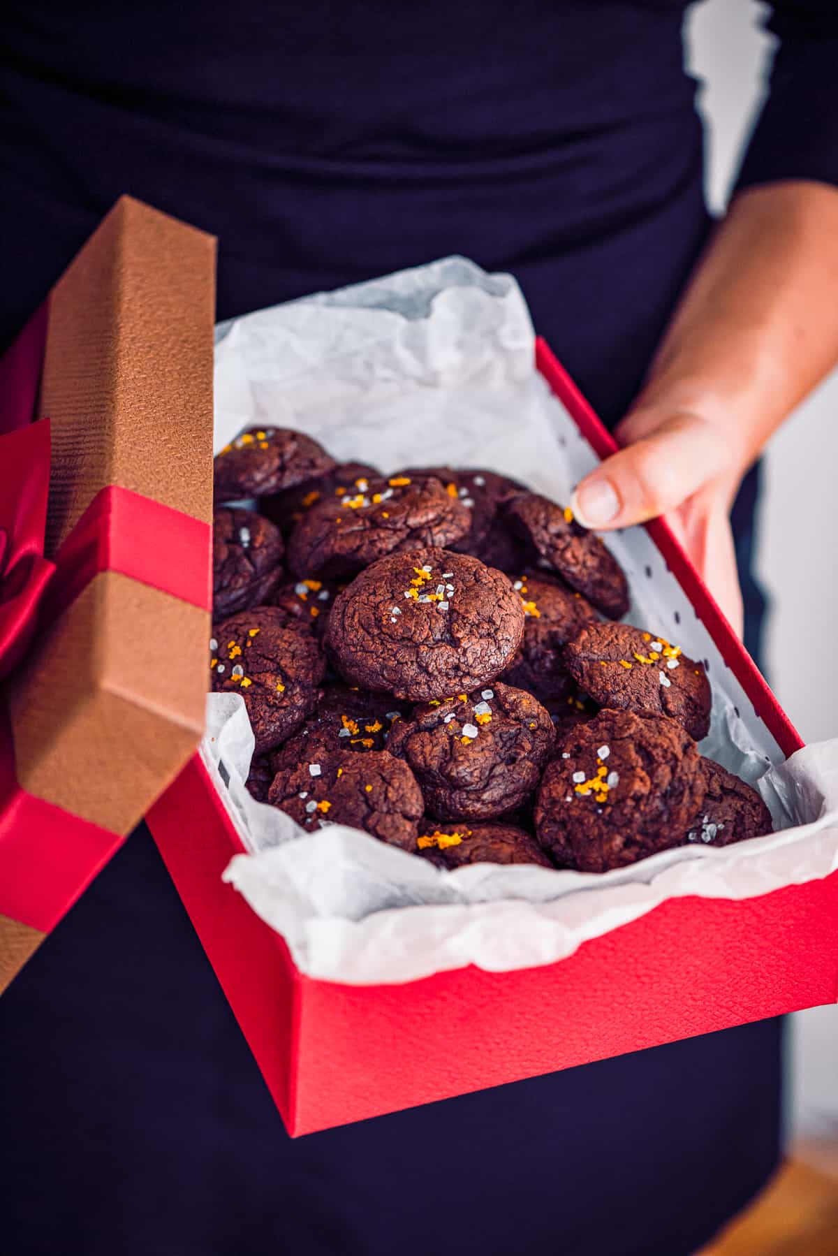 Woman holding a red gift box full of chocolate cookies.