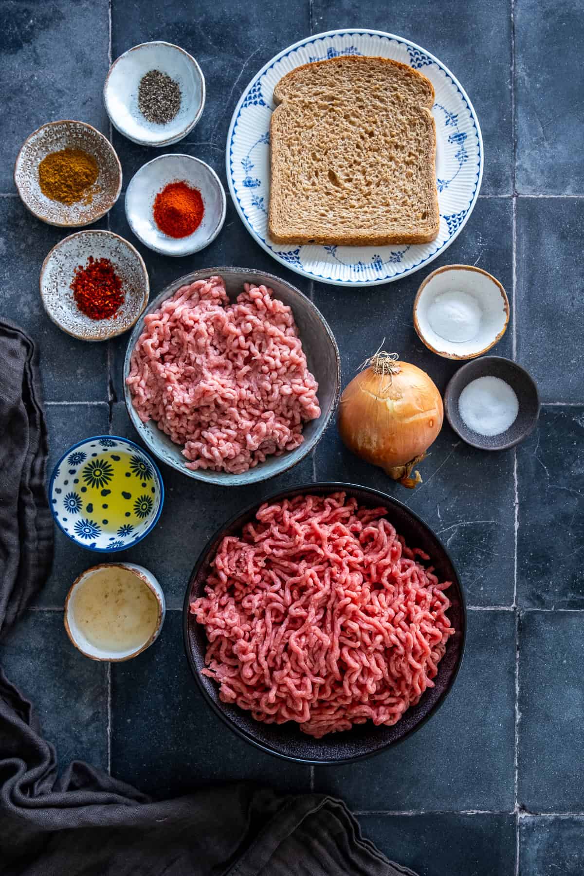 Overhead view of ingredients for Turkish şiş köfte, including ground beef, ground lamb, bread, onion, olive oil, vinegar, baking soda, salt and spices.