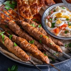 Turkish şiş köfte (meatball skewers) served on a platter with pide bread, white bean salad topped with boiled eggs, and fresh parsley.