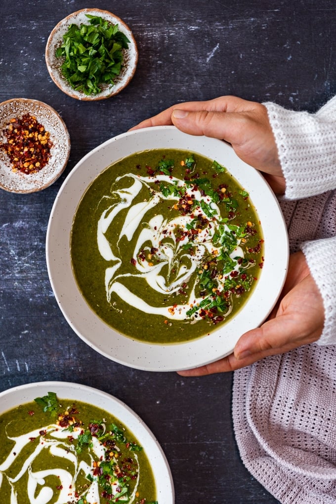 Woman serving lentil spinach soup with vegan cream, parsley and red pepper flakes topping in two bowls