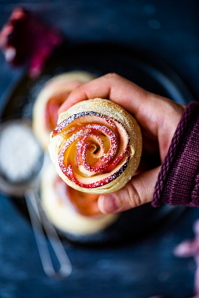 Holding a mini apple rose tart with powdered sugar