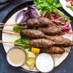 Kofta kebab served on lavash with sumac onions, tahini sauce and yogurt sauce.