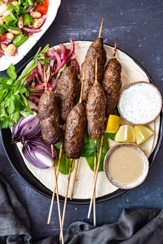 Kofta kebab served on lavash with sumac onions, tahini sauce and yogurt sauce on the side.