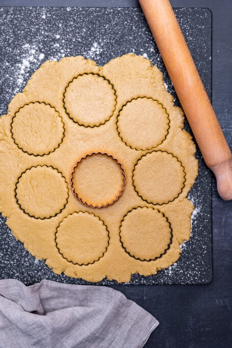 Cookie dough rolled out and cut with a round cookie cutter and a rolling pin on the side.