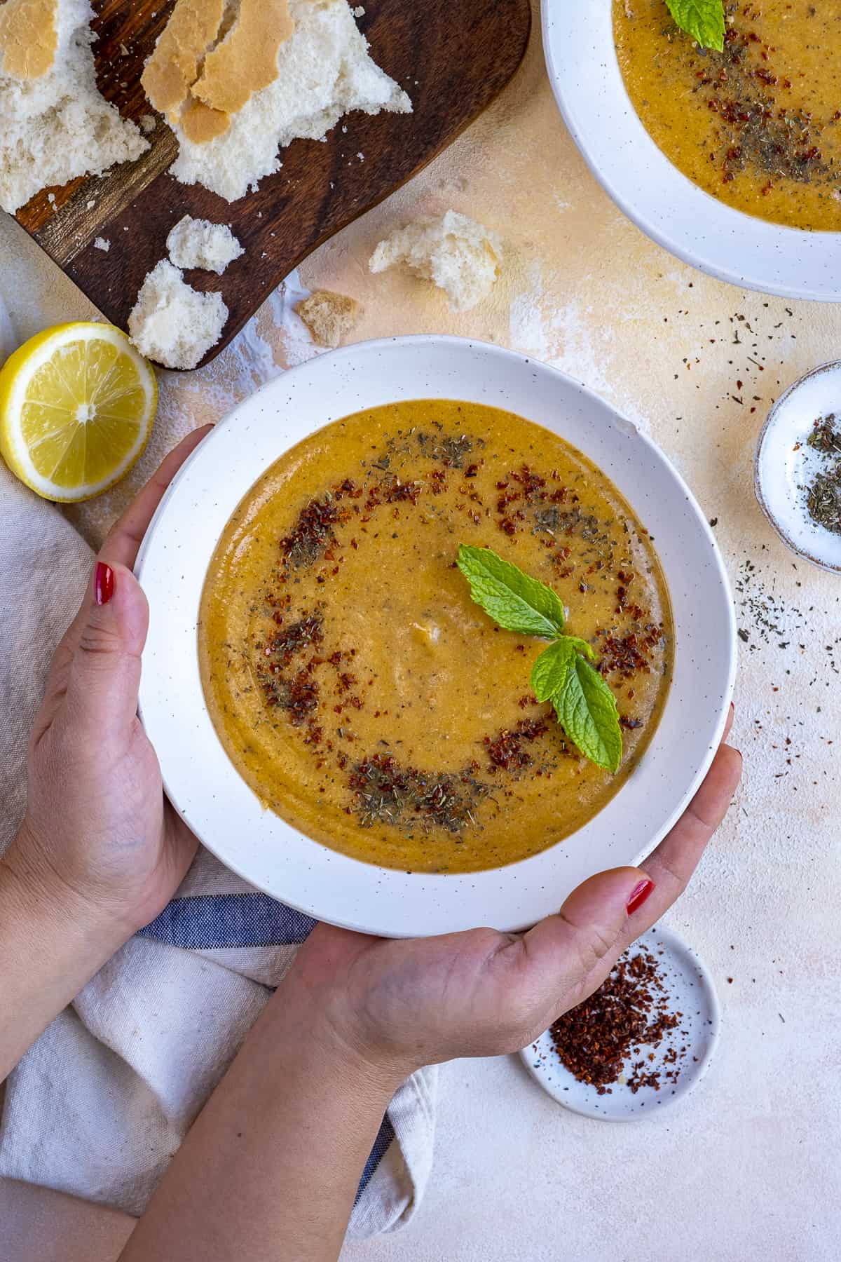 Hands holding a bowl of lentil soup garnished with fresh mint and spices.