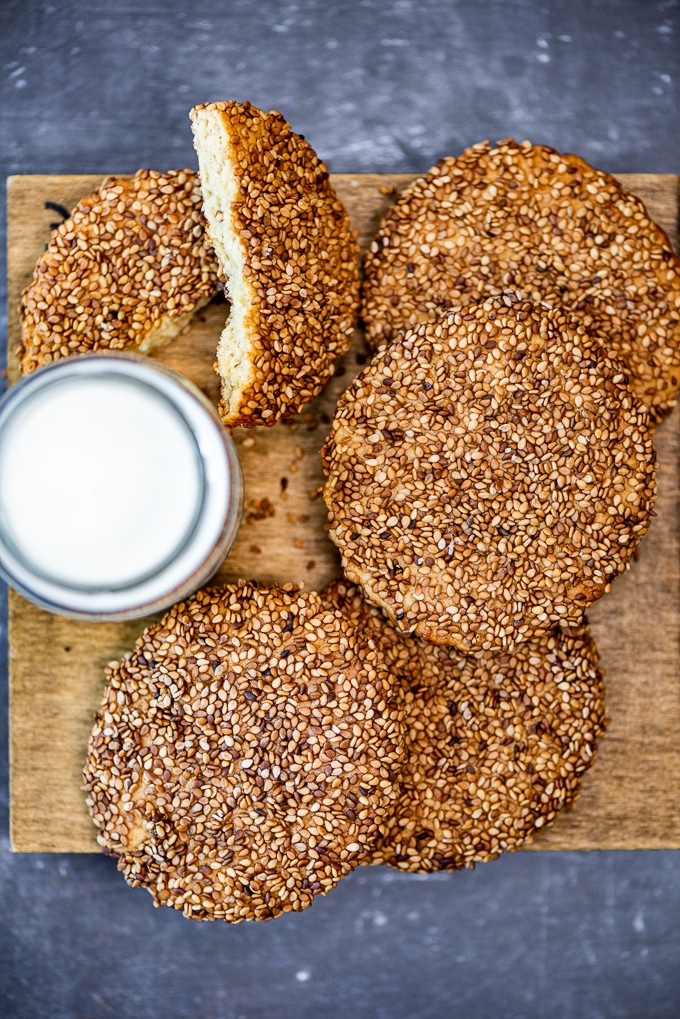 Large Turkish tahini sesame cookies on a wooden board and a glass of milk on the side.
